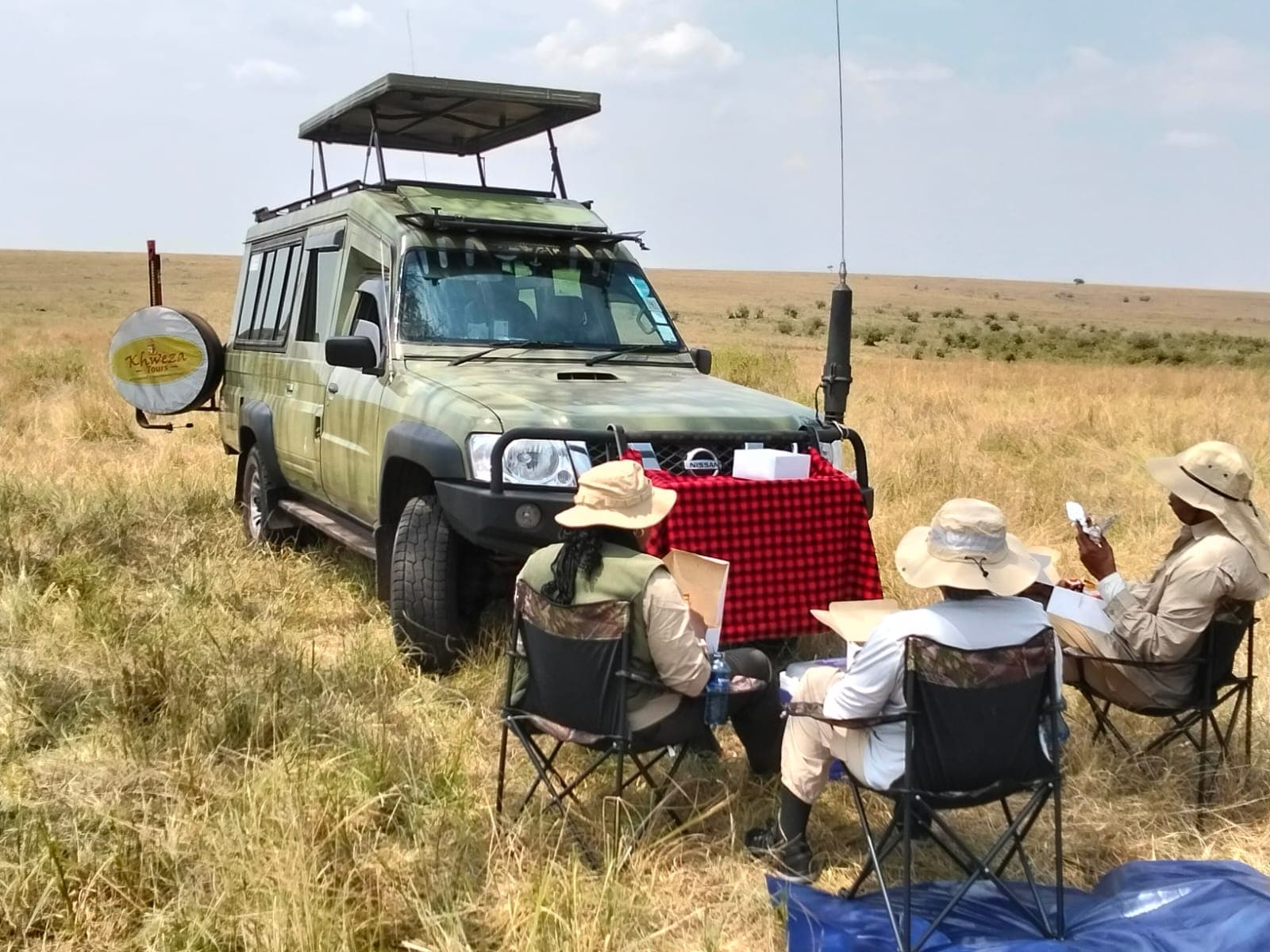 Guests enjoying a bush lunch beside a Khweza vehicle on the Maasai Mara plains