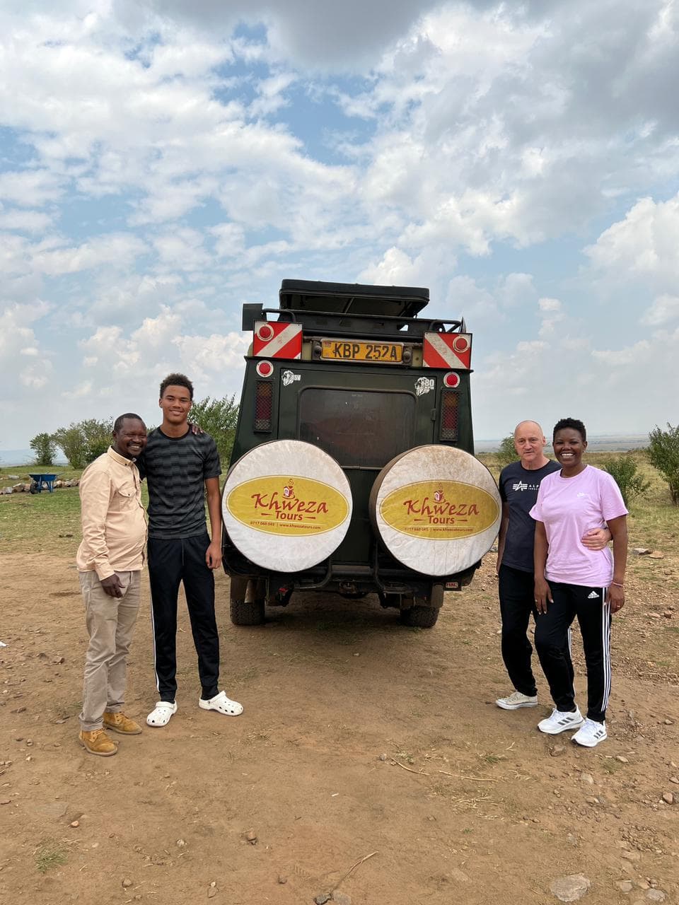 Khweza guide and guests standing behind a safari vehicle in the Maasai Mara